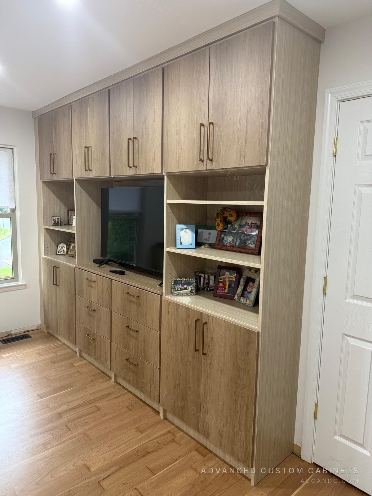 Bedroom media wall in a light wood finish with upper cabinets, a TV niche, open display shelves and drawer bases