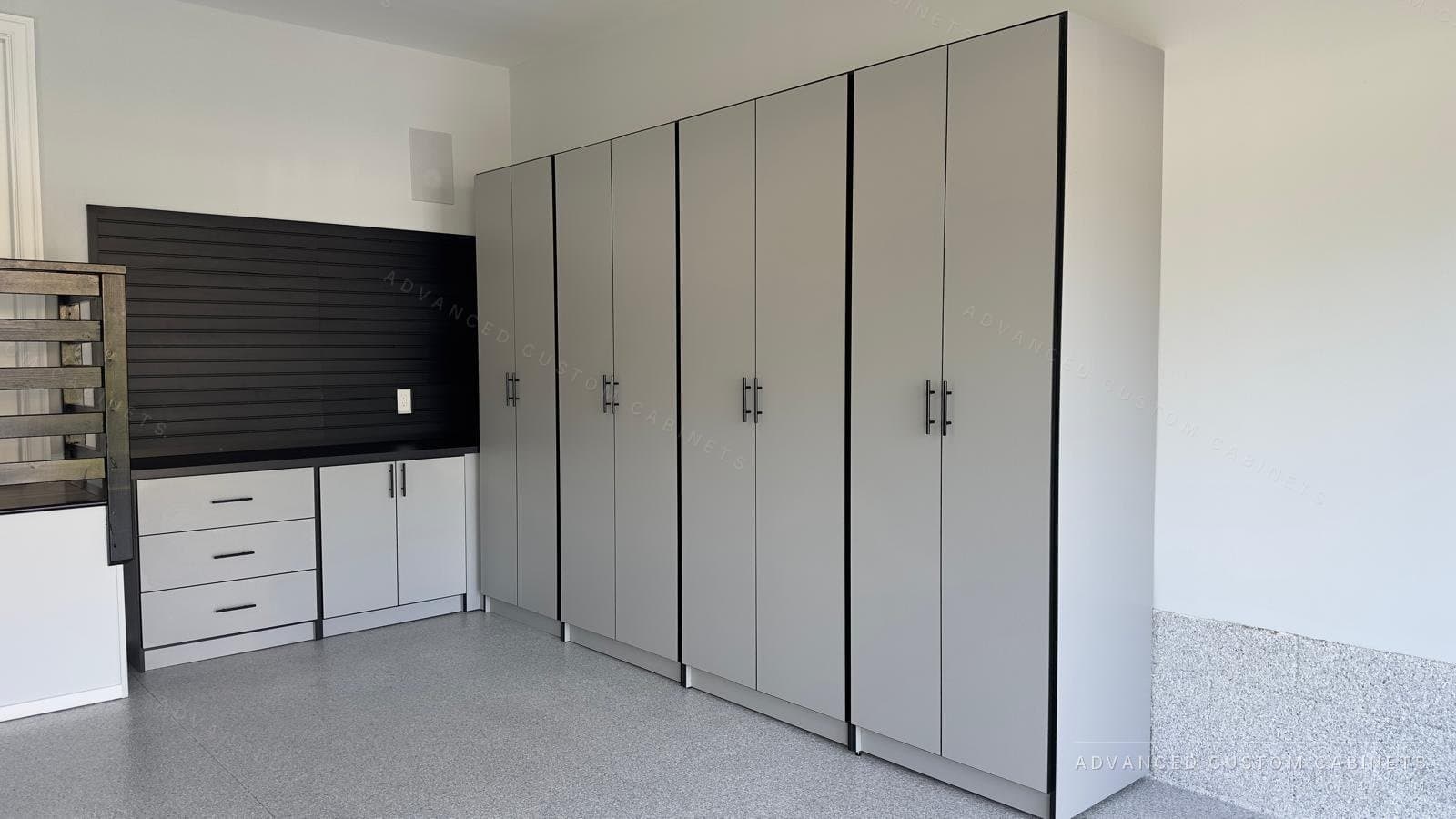 Custom garage storage with full-height white cabinets, a black slatwall panel, a countertop workspace, and an epoxy floor