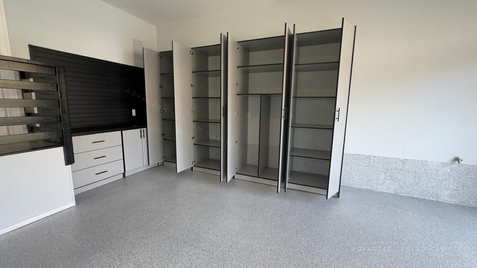 Custom garage cabinets shown open, with adjustable shelving, a drawer base, and black slatwall organizer panels