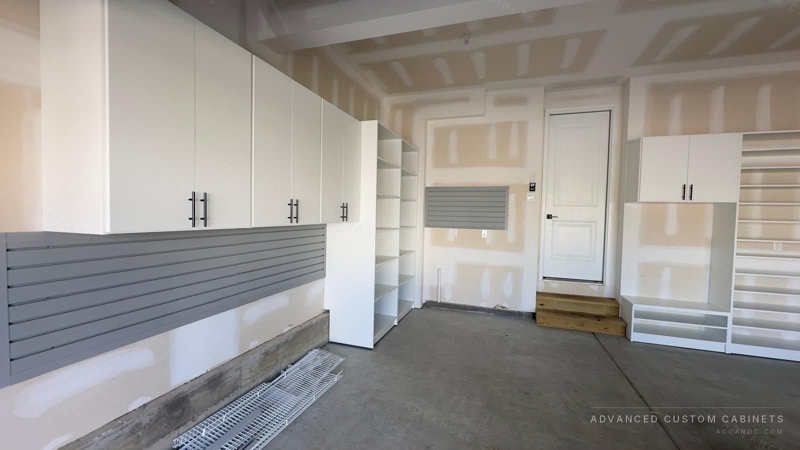 Custom garage with white wall-mounted upper cabinets, an open shelving tower, and gray slatwall organizer panels