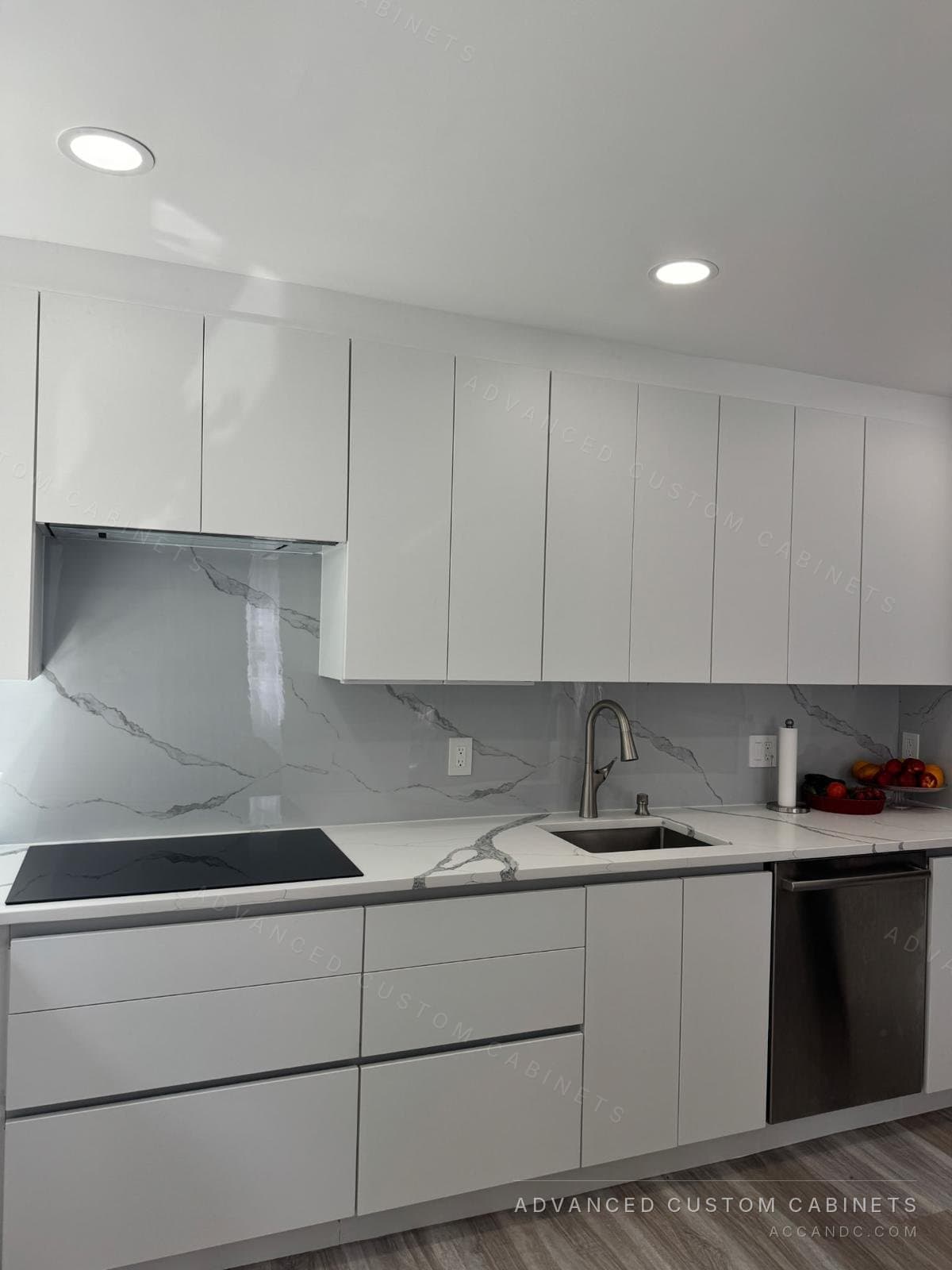 Modern white flat-panel kitchen with induction cooktop, concealed range hood, marble-look quartz backsplash, and undermount sink