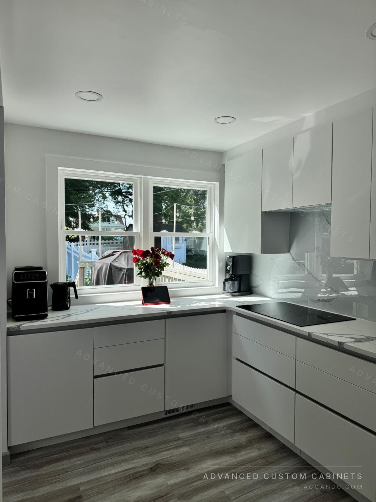 Modern white kitchen corner with L-shaped quartz counters, induction cooktop, and a picture window over the counter