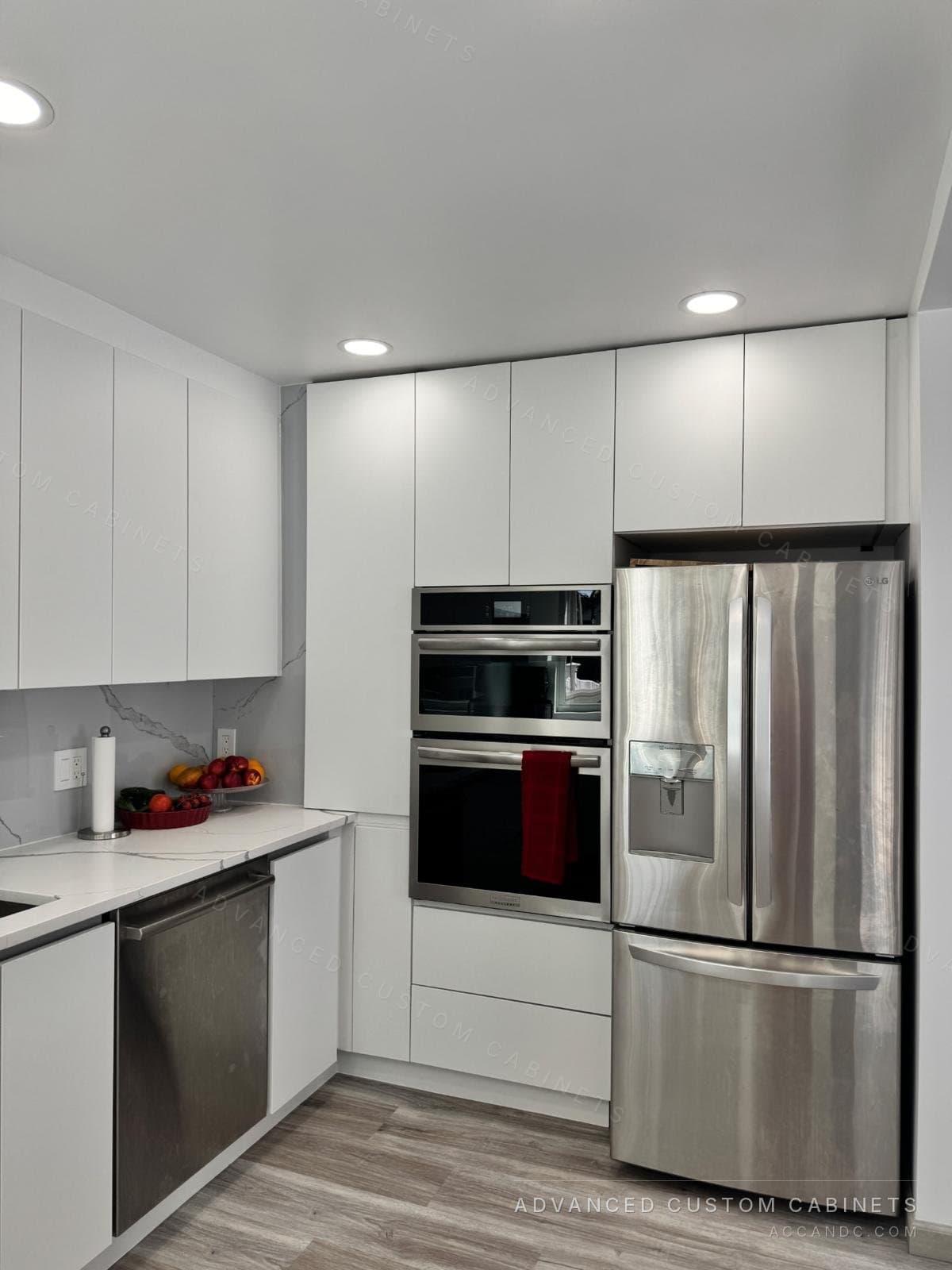 Modern white handleless kitchen with full-height cabinets, a built-in double wall oven, stainless refrigerator, and marble-look quartz counters