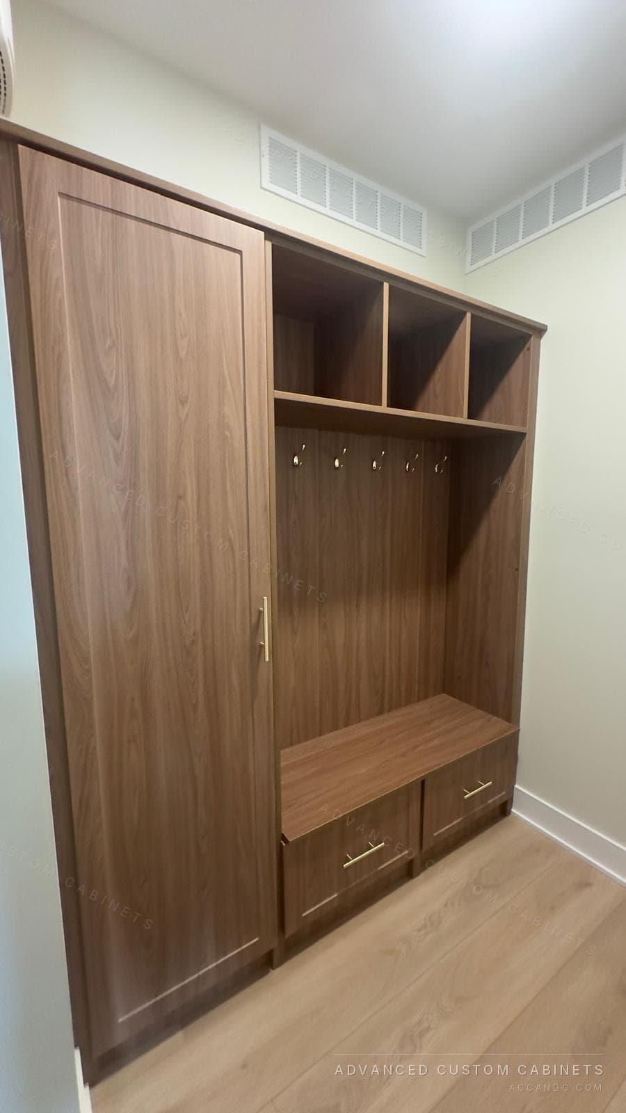 Custom walnut-finish mudroom locker with a tall wardrobe cabinet, open cubbies, brass coat hooks, and a storage bench with drawers