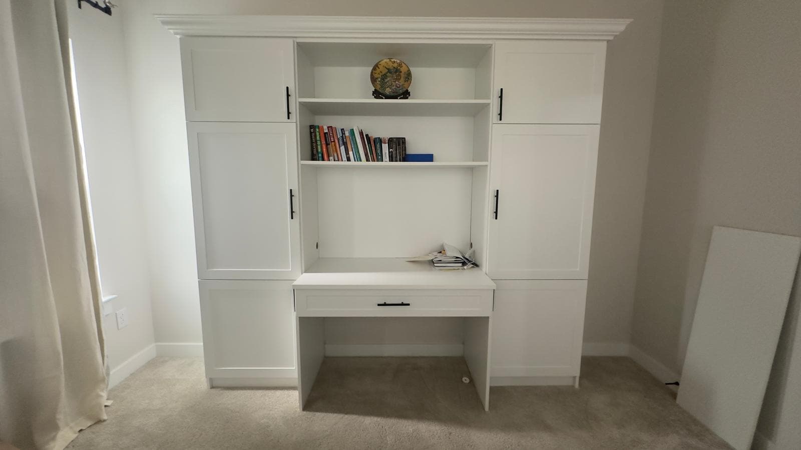 Custom white built-in home office with central desk and drawer, open bookshelves, flanking tall cabinets, and crown molding