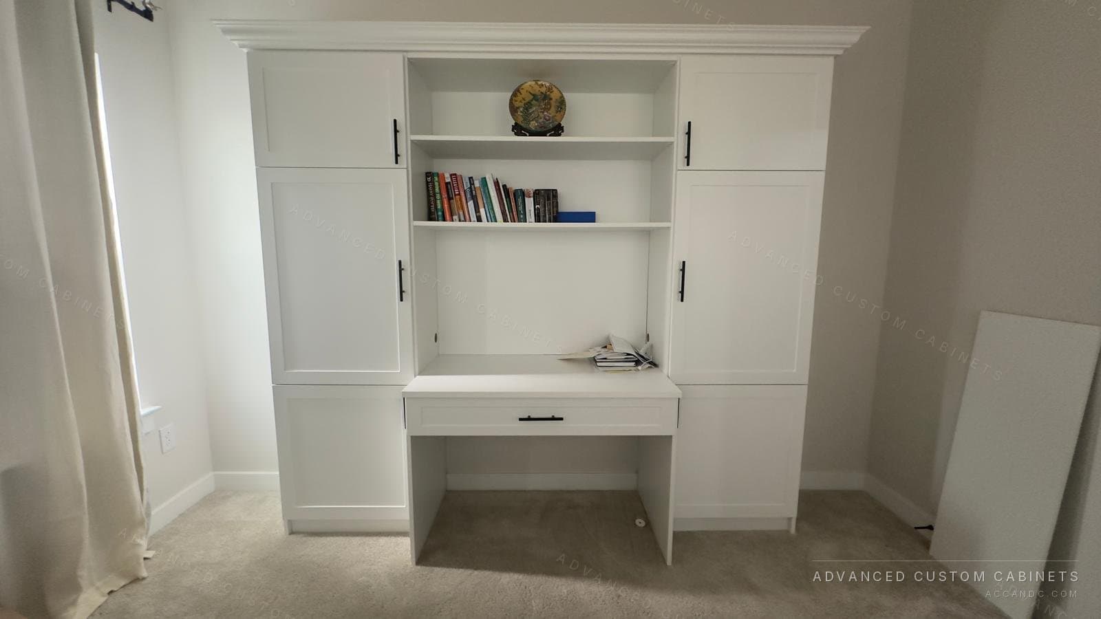 Custom white built-in home office with central desk and drawer, open bookshelves, flanking tall cabinets, and crown molding