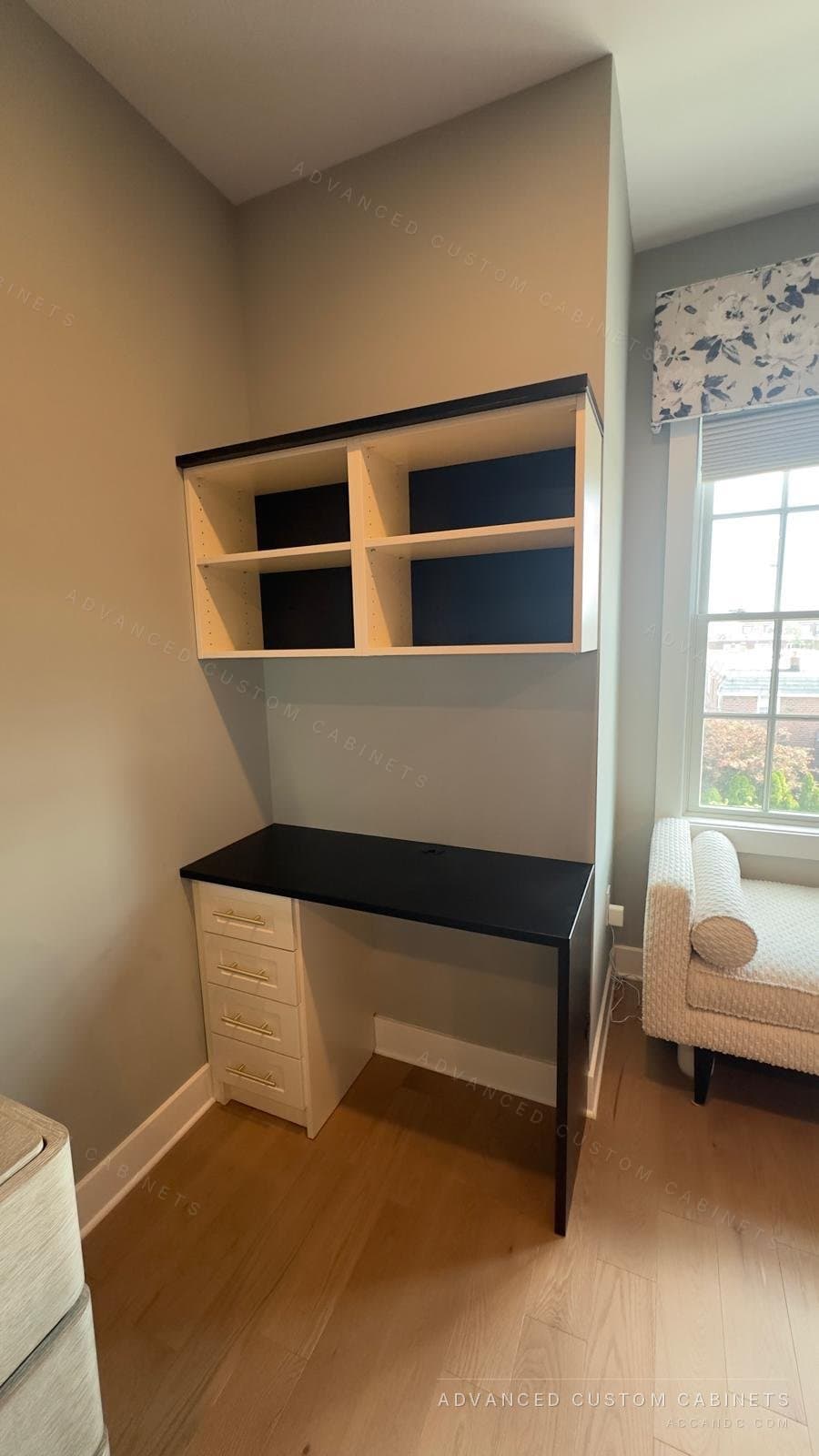 Custom home office desk with a black work surface, a drawer base, and open upper cabinets set beside a bedroom window