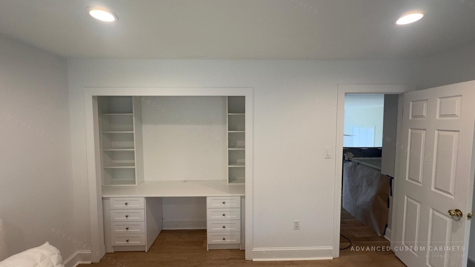 Recessed custom home office desk with flanking drawer bases, open upper shelving, and a white painted finish
