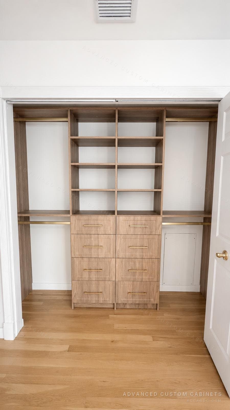 Custom light oak-finish reach-in closet with central open-shelf tower, two four-drawer bases with brass bar pulls, and dual hanging rods over hardwood flooring