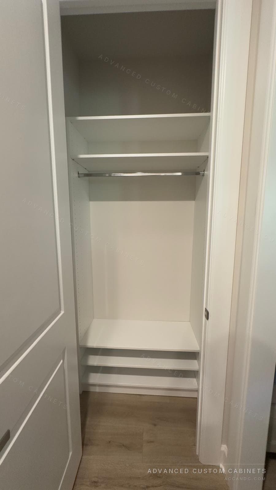 White reach-in closet with a single shelf and hanging rod behind a hinged door