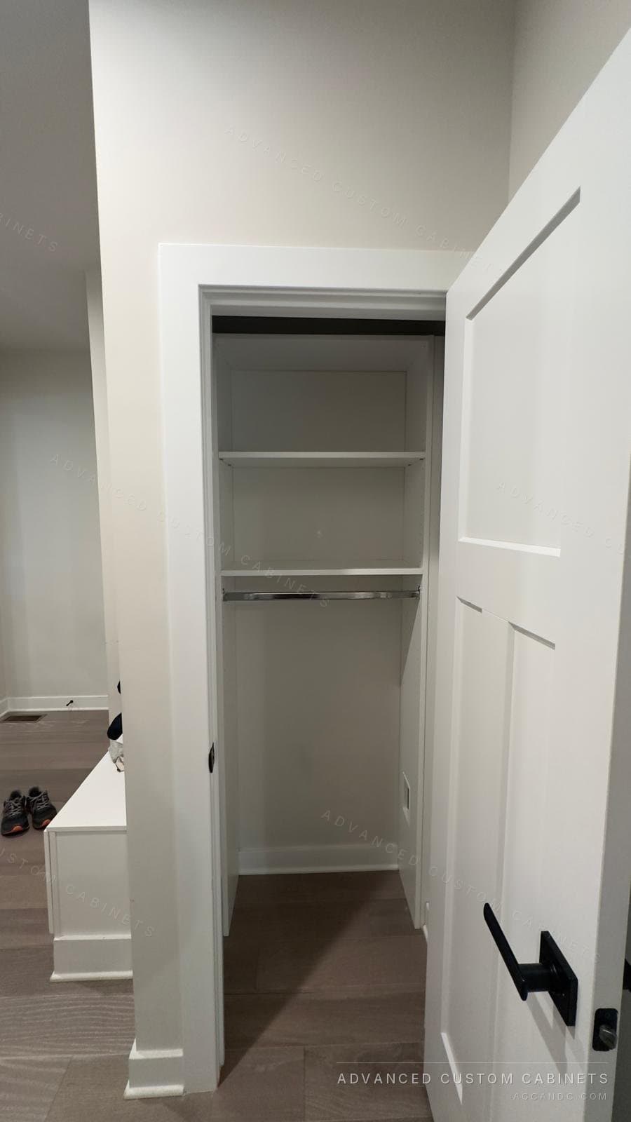 Small white reach-in closet with a hanging rod under two shelves behind a white shaker door
