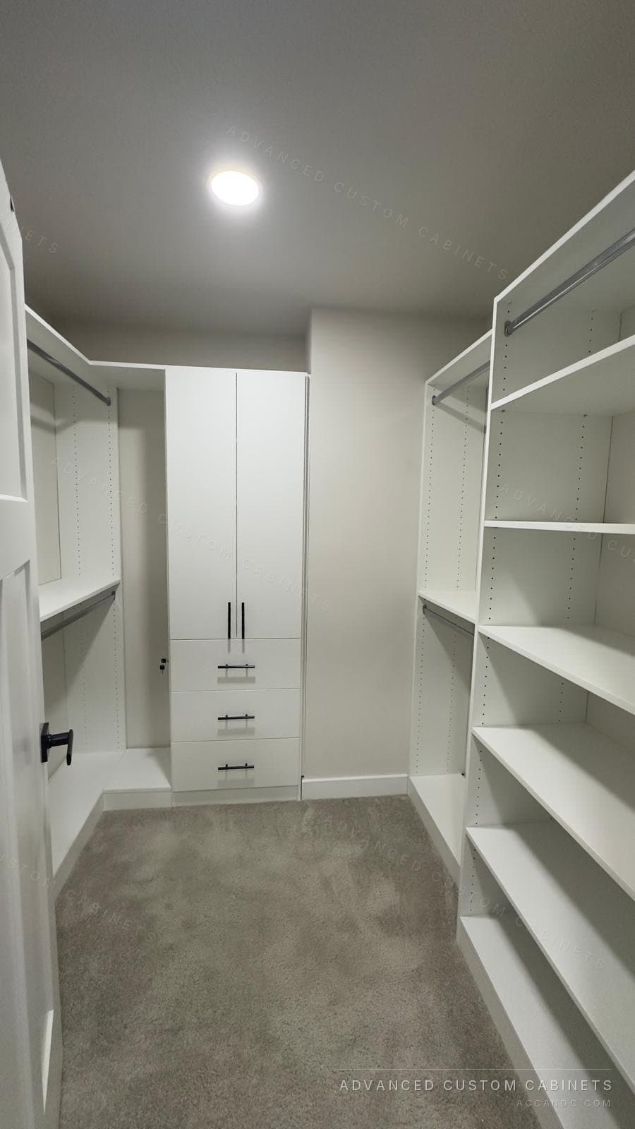 White walk-in closet with shelving along both walls, a centre cabinet with drawers and full-length hanging