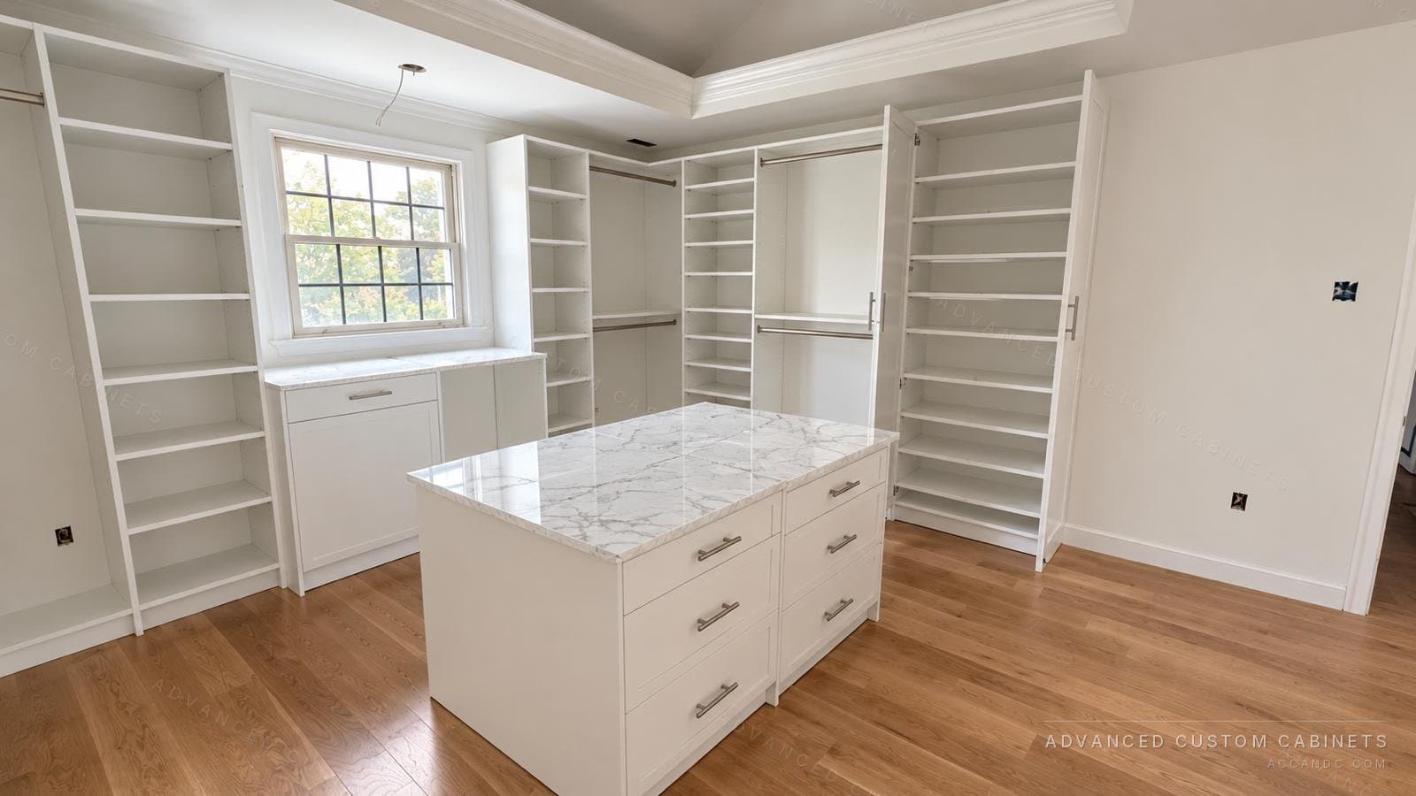 White walk-in closet with a marble-top island of six drawers, floor-to-ceiling shelving, double hanging rods and a vanity counter under the window