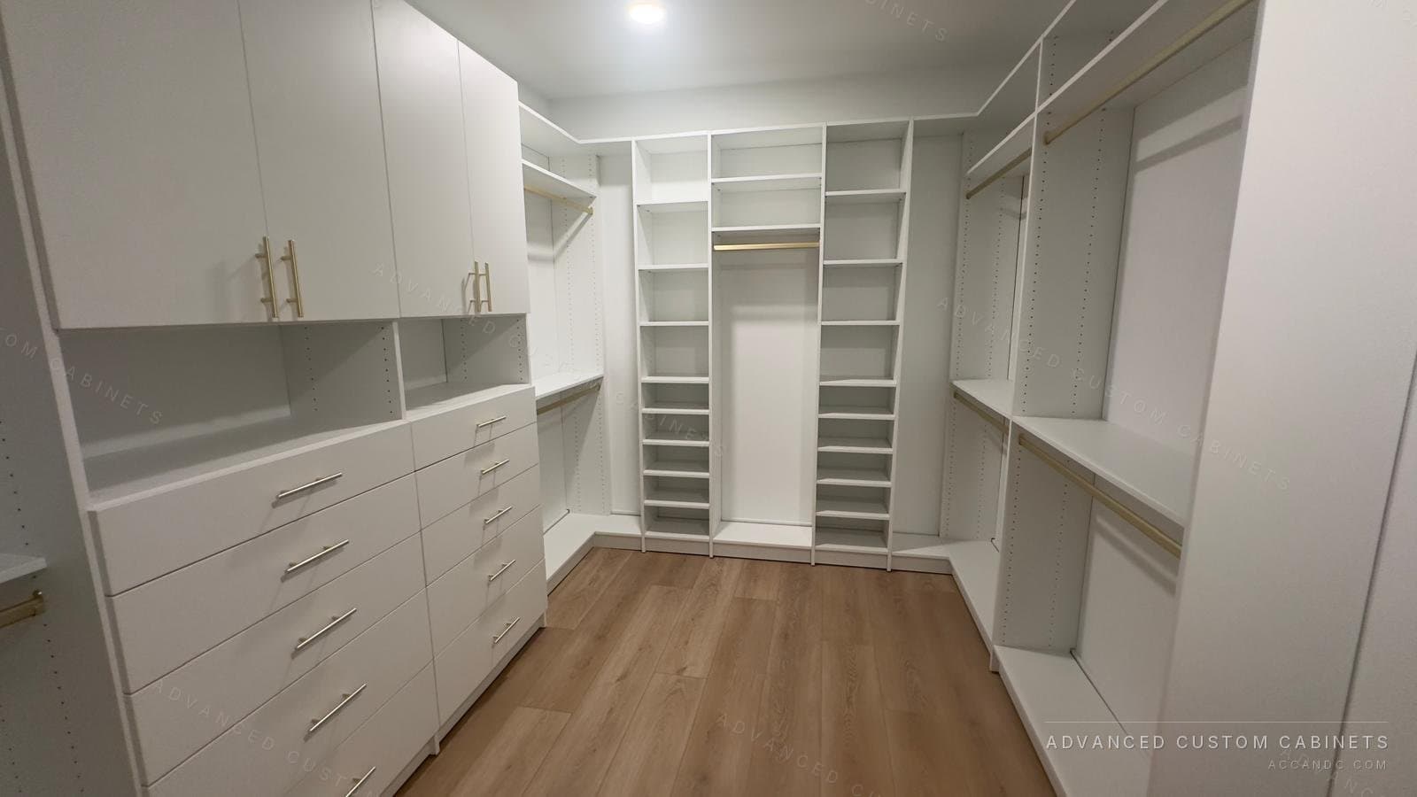Custom white walk-in closet with U-shaped adjustable shelving, brass rods, tall cabinets, and a bank of drawers
