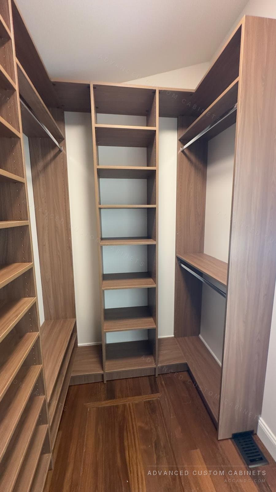 Walnut-finish custom walk-in closet with a center shelving tower, double hanging rods on the right, and floor-to-ceiling shelves on the left