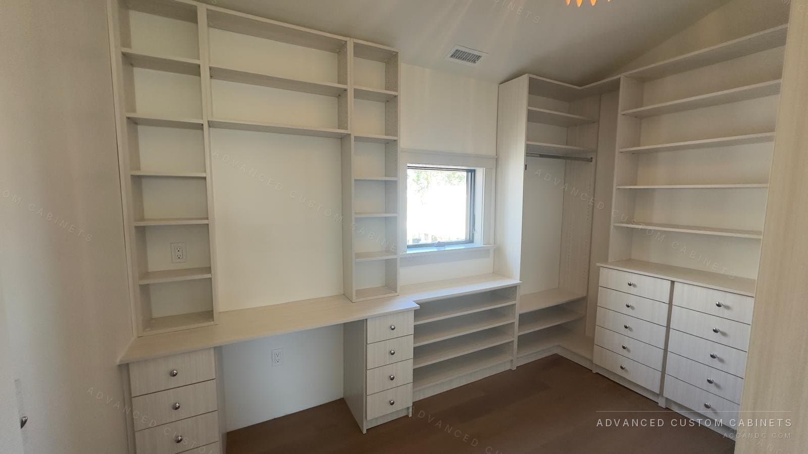 Custom white walk-in closet with a built-in desk, floor-to-ceiling open shelving, drawer banks, and a window seat