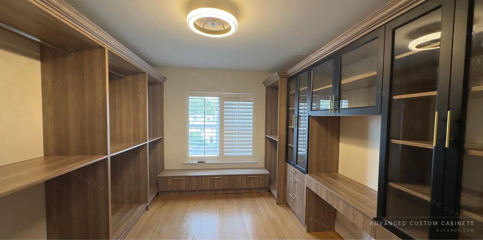 Wood-finish custom walk-in closet with a built-in window bench, a desk run, and black glass-front display cabinets