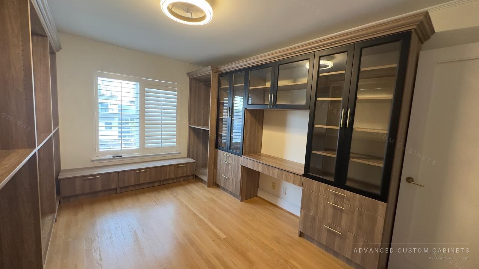 Custom walk-in closet with black glass-front display cabinets, a built-in desk, window bench, and wood open shelving