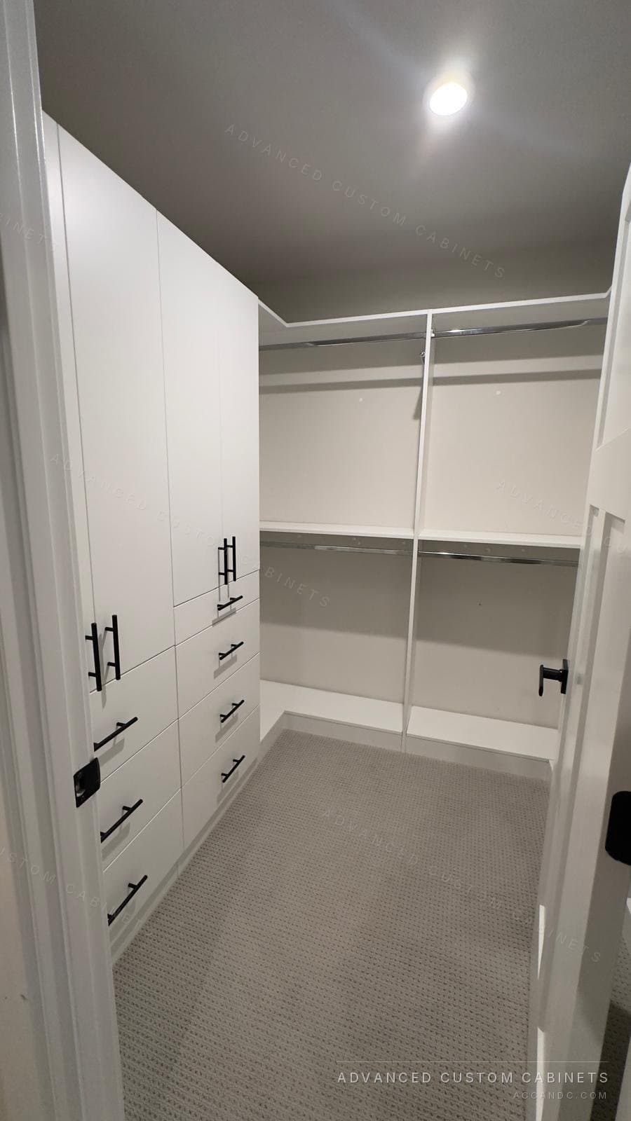 White walk-in closet with tall door cabinets over drawers with black bar pulls on one wall and double hanging along the back