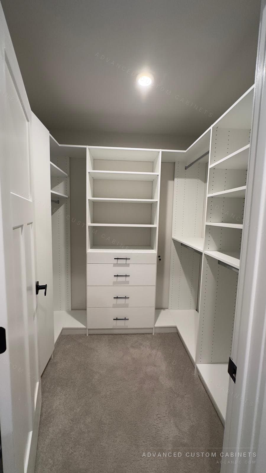 Narrow white walk-in closet with hanging rods and adjustable shelves along both walls and a back tower of open shelves over five drawers