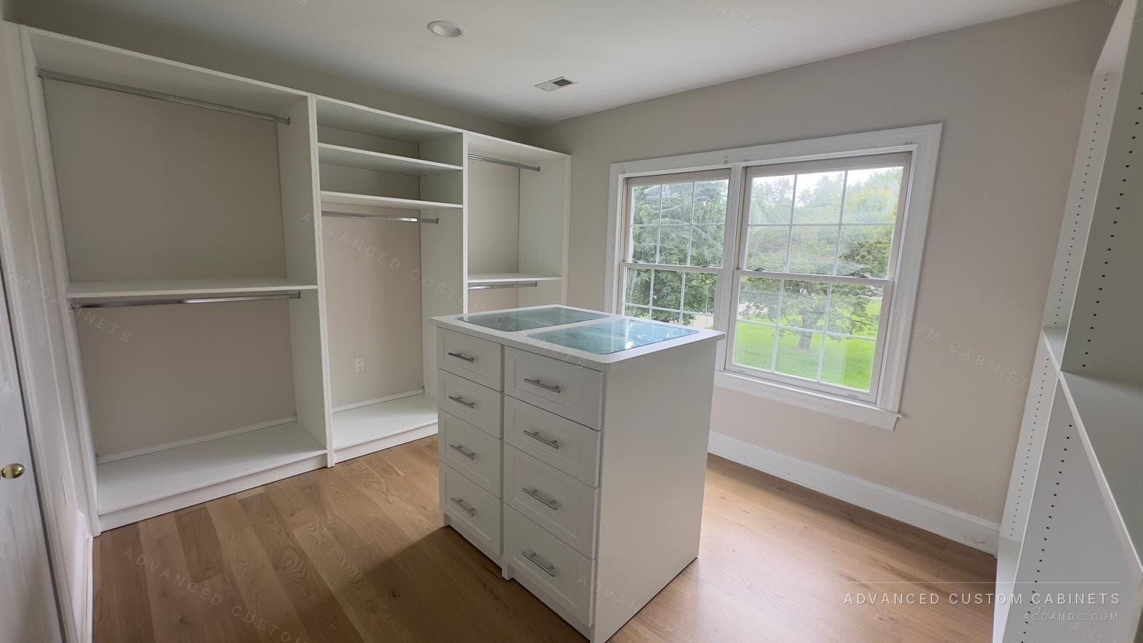 Custom white walk-in closet with a freestanding drawer island under a glass display top and hanging sections along both walls