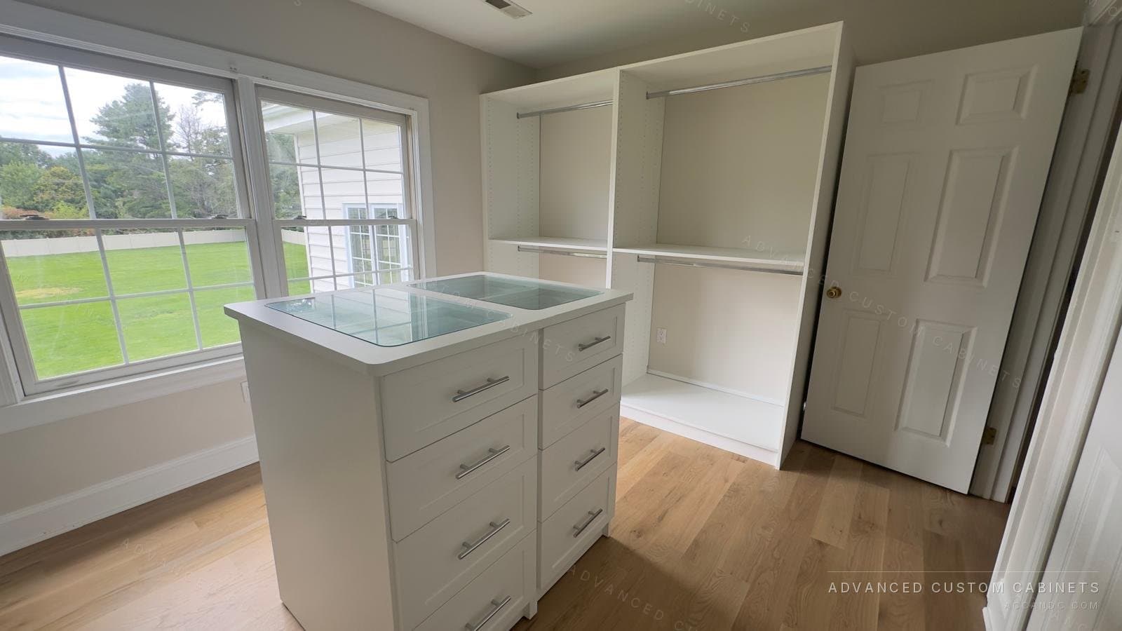 Custom walk-in closet island with a glass display top and six drawers, set between corner windows and open hanging shelves