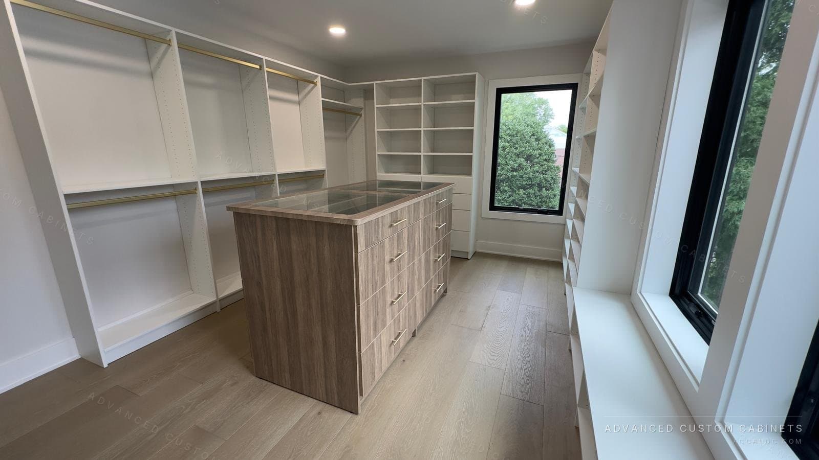 Custom walk-in closet with a wood-finish drawer island, floor-to-ceiling windows, and open white shelving along both walls