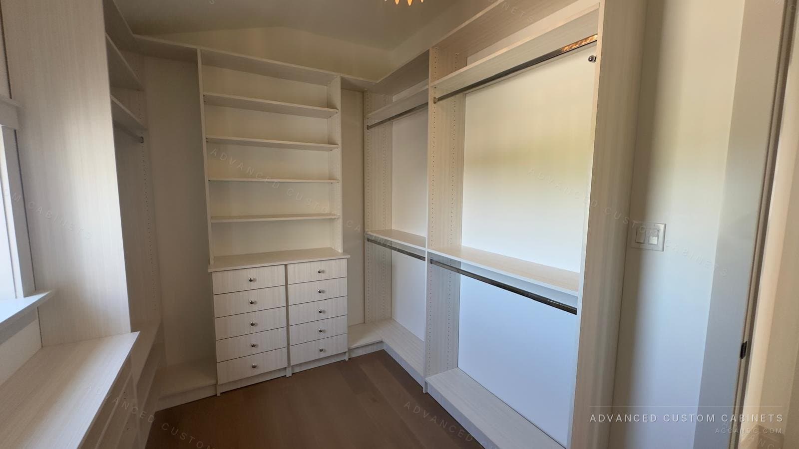 Custom white walk-in closet with open display shelving, a five-drawer base, chrome hanging rods, and a window bench