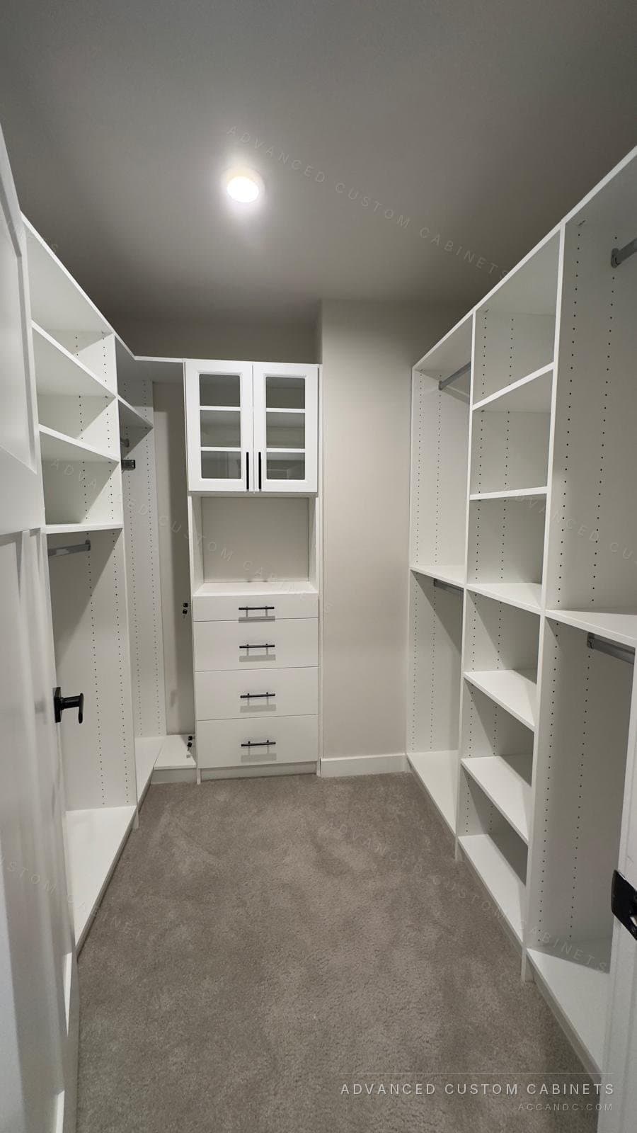 White walk-in closet with glass-front upper doors over a four-drawer base on the back wall and open shelving and hanging towers down both sides