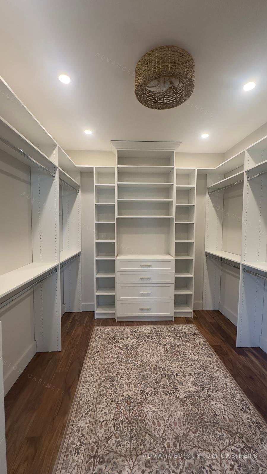 Custom white walk-in closet with dual-wall hanging and adjustable shelving, a central drawer tower, and a patterned runner over hardwood