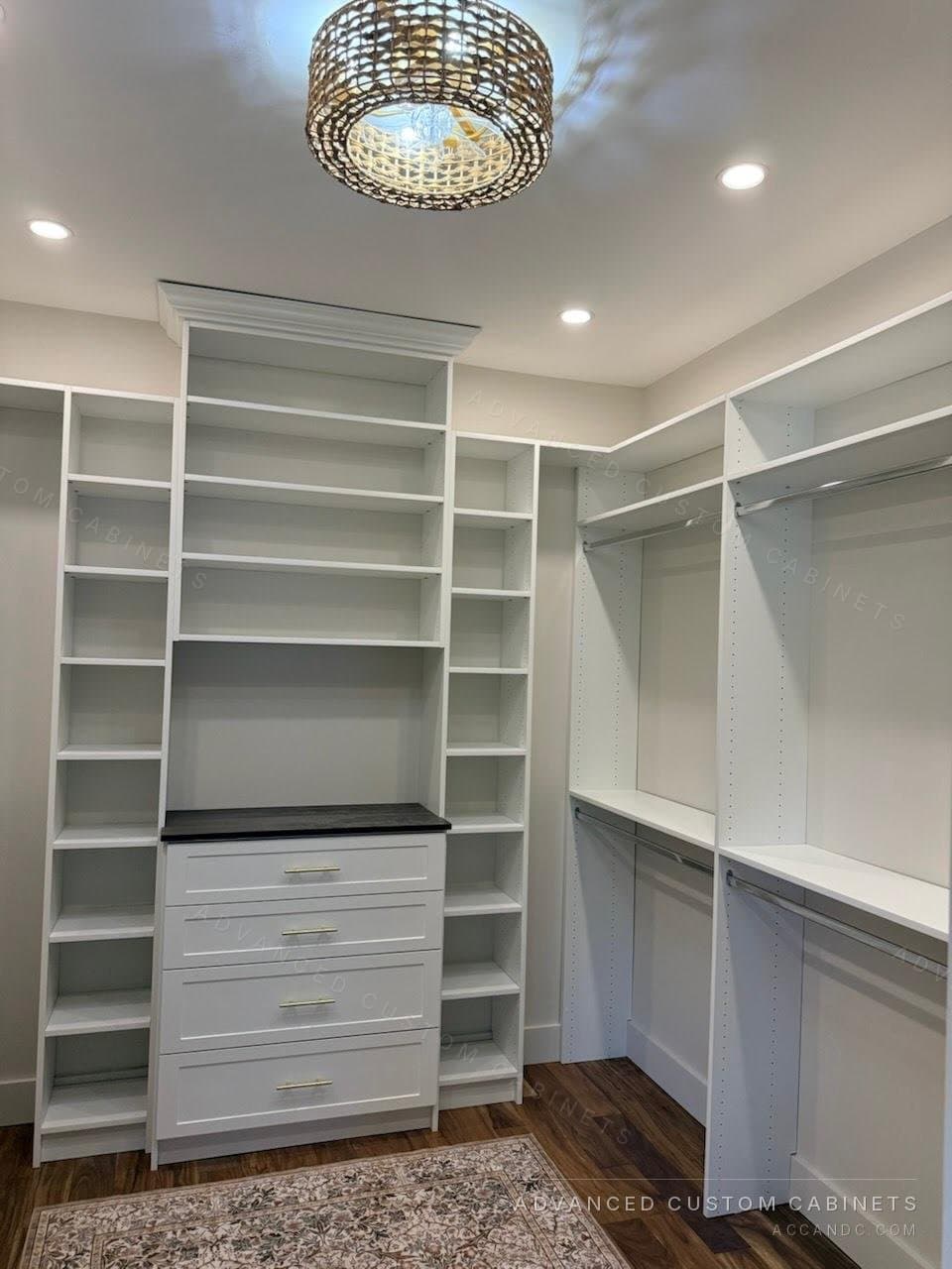 Custom white walk-in closet with crown molding, a drawer tower with a dark counter, tall shelving, and a woven chandelier