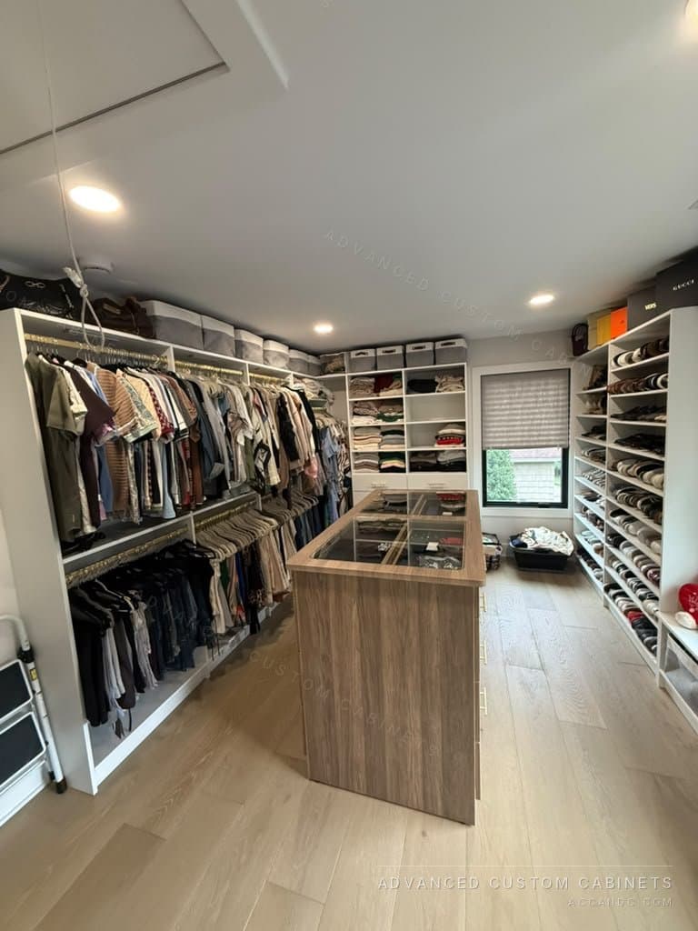 Large custom white walk-in closet fully outfitted with hanging sections, a wood-finish center island, built-in shoe shelving, and open sweater shelves