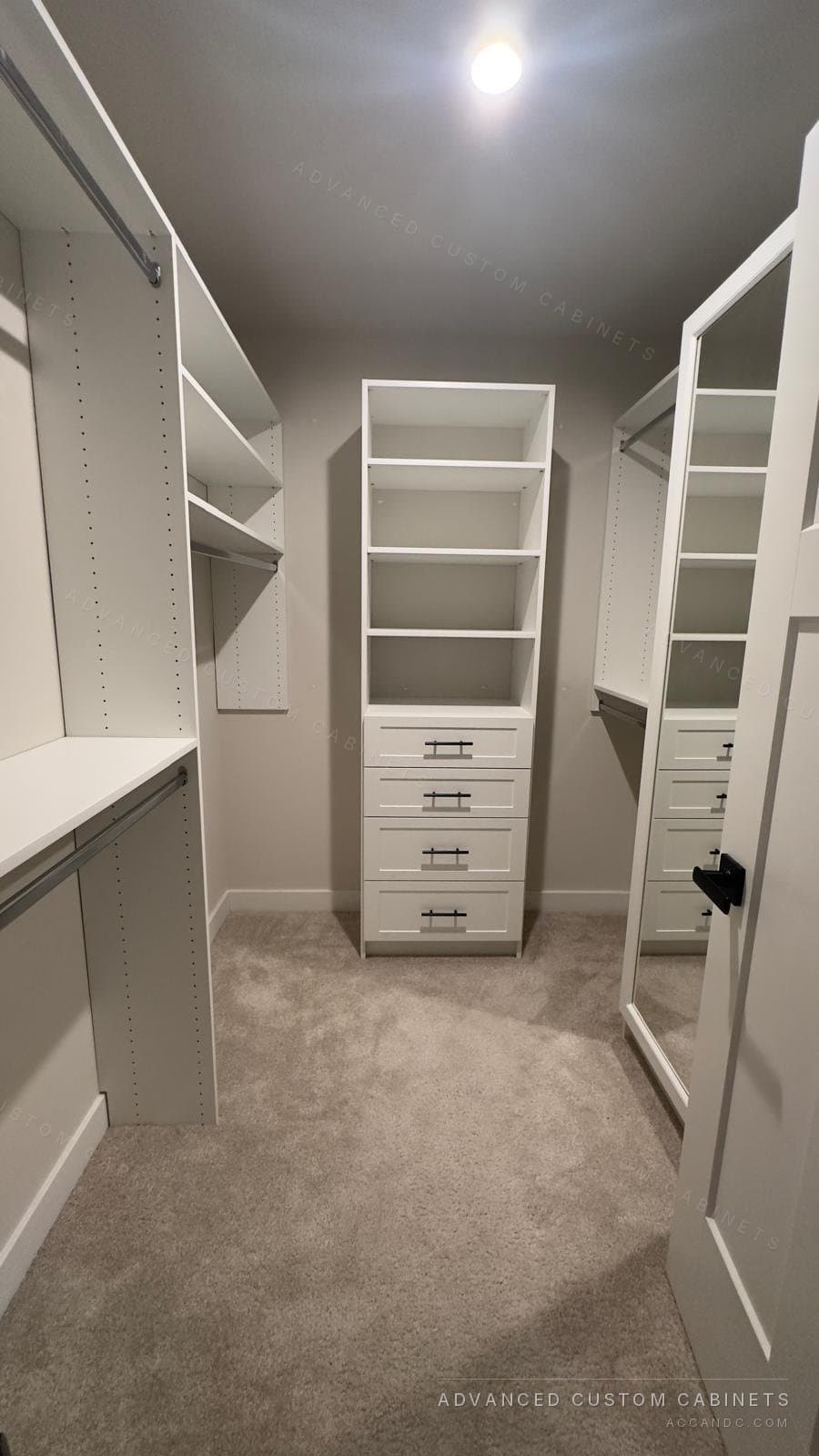 Narrow white walk-in closet with central open-shelf tower over a four-drawer base, side hanging rails, and a full-length mirrored door