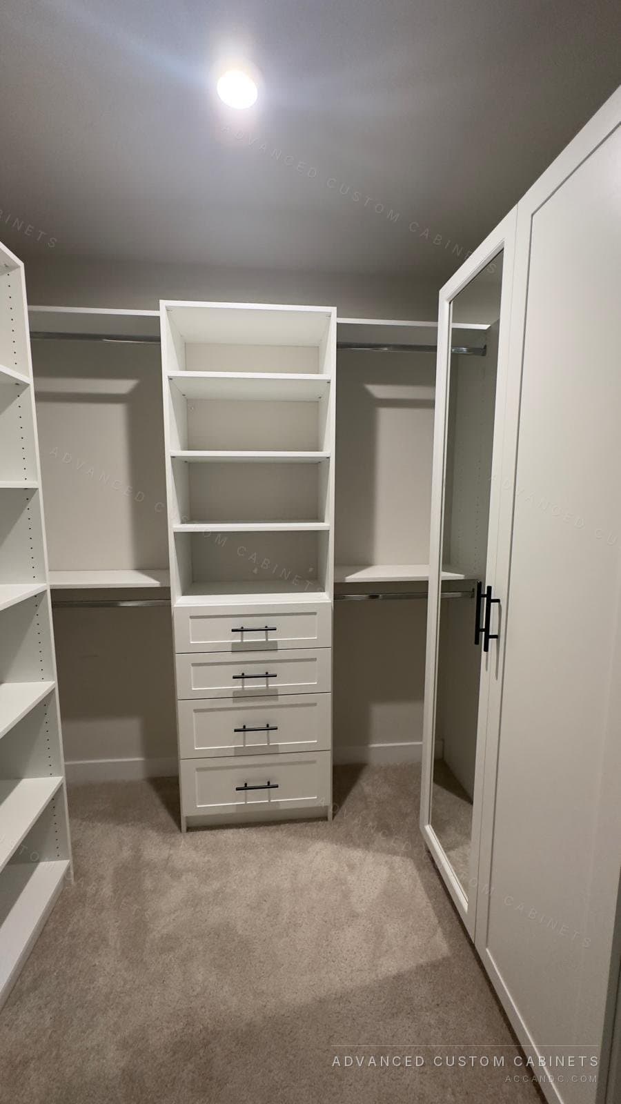 Custom white walk-in closet with a central drawer tower, adjustable shelving, double hanging rods, and a mirrored door