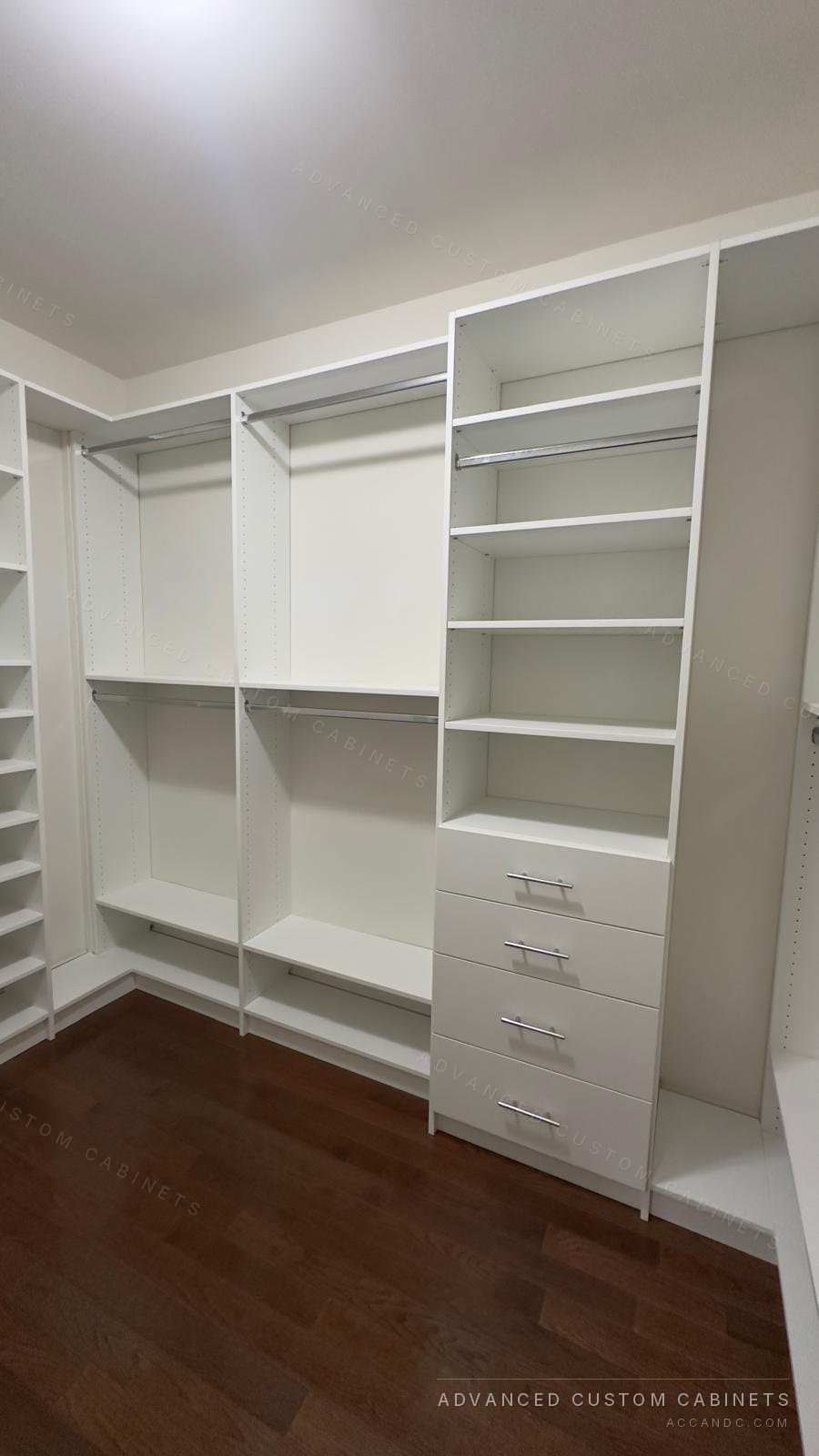 Custom white walk-in closet with double hanging sections, a tall shelving tower over a four-drawer base with chrome pulls, and shoe shelves on the left
