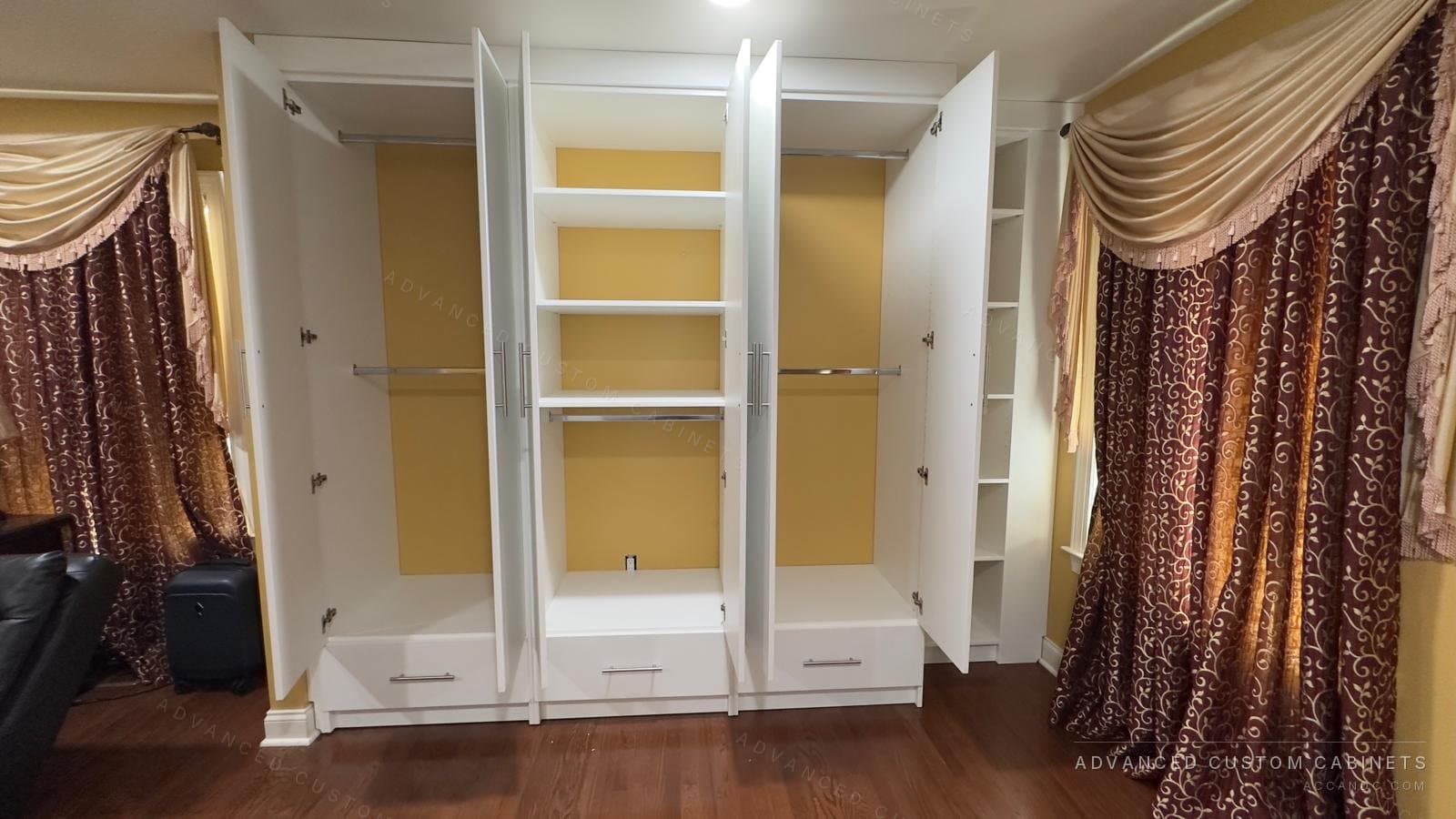 Open white wardrobe interior with three hanging sections, upper shelves and a four-drawer centre unit