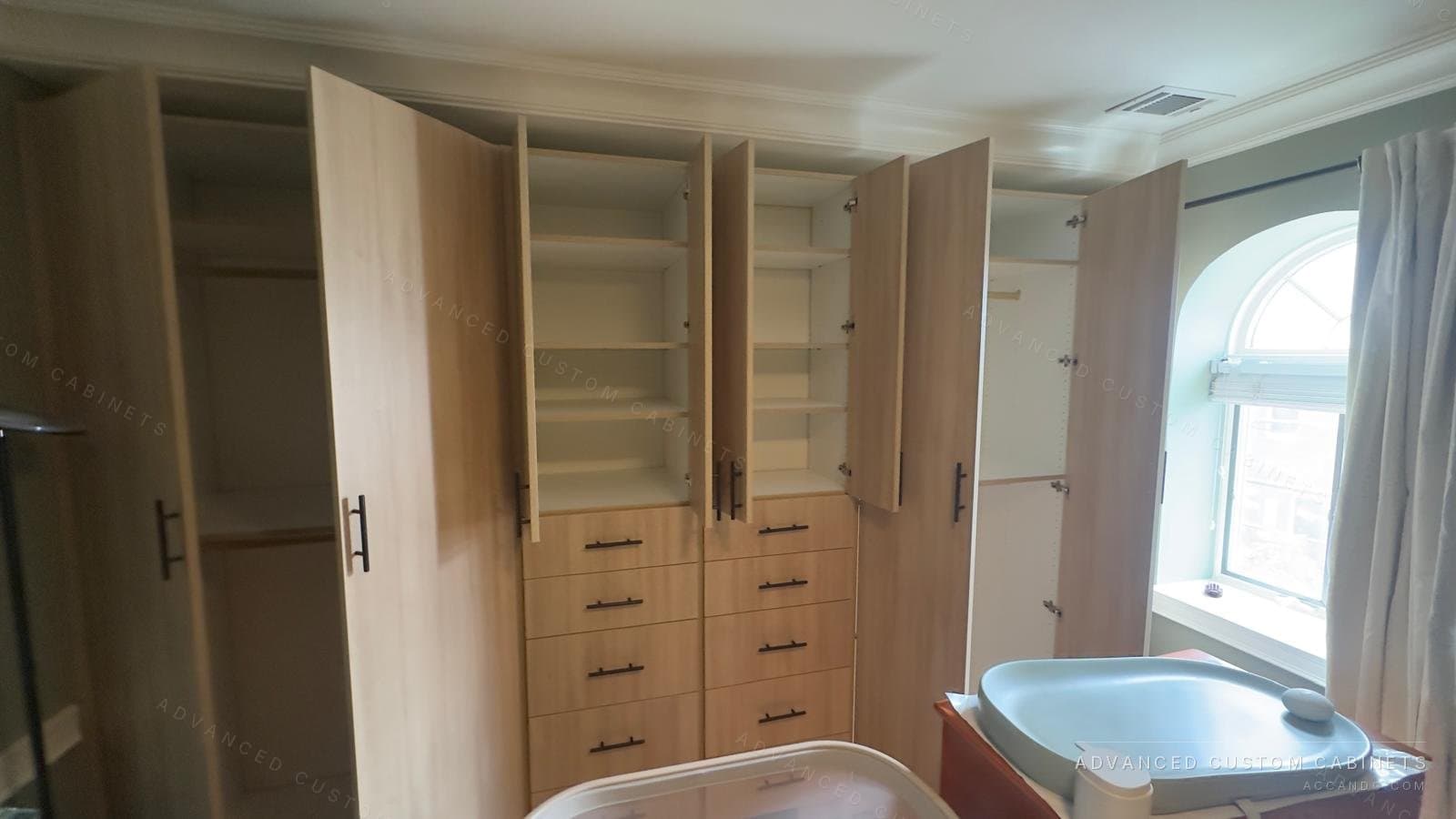Light oak wardrobe wall with the doors open, showing adjustable shelves, hanging sections and two four-drawer stacks